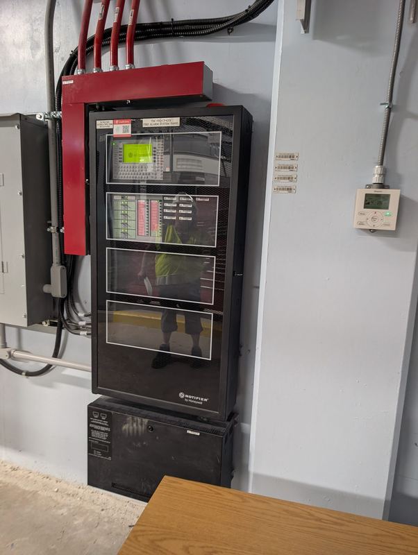 Addressable fire alarm control panel with red conduit feeds in a utility room.